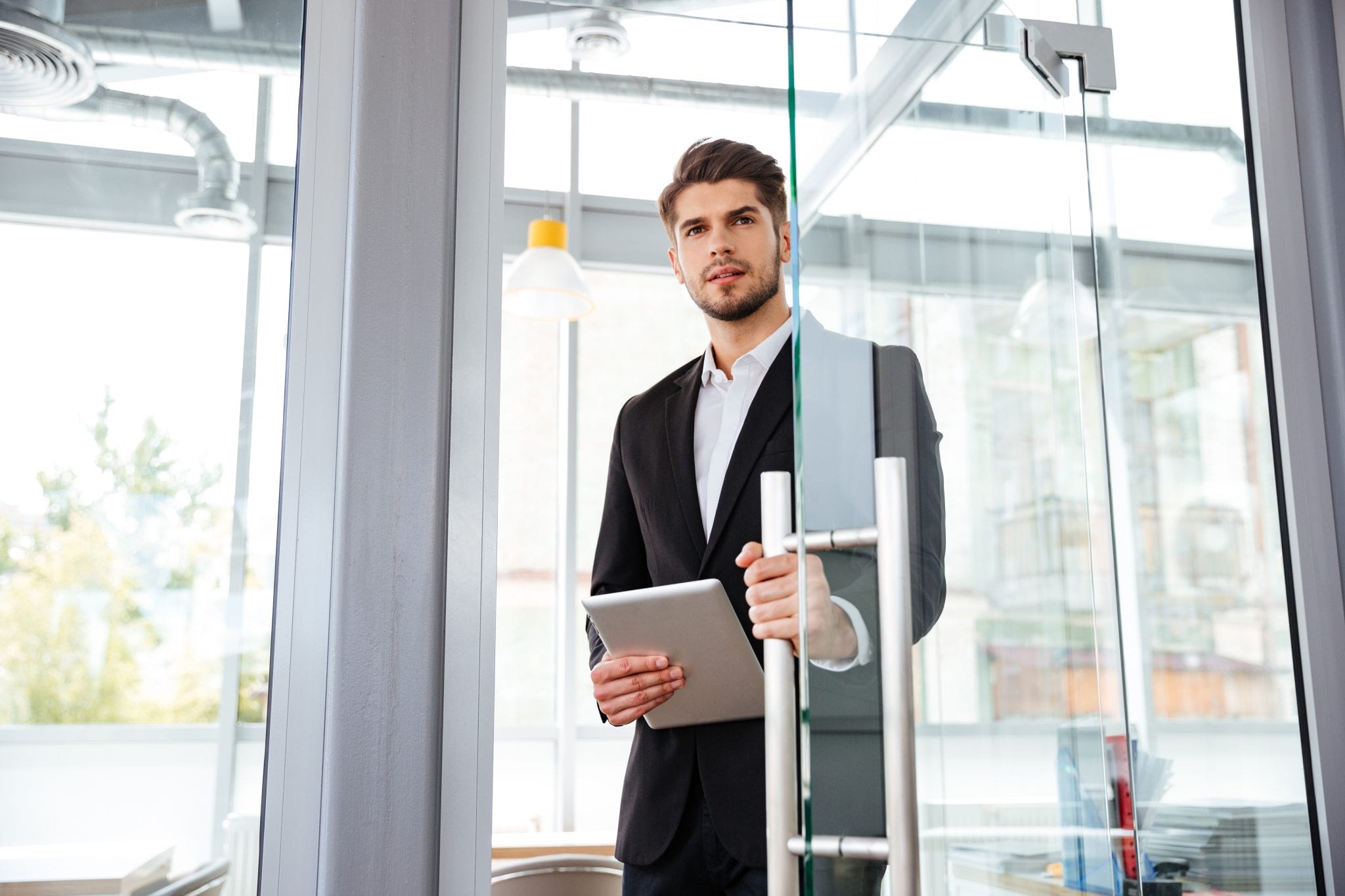 Handsome young businesman with tablet entering the door in office